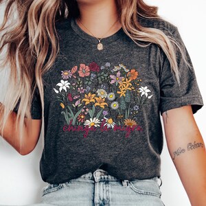 Może przedstawiać: Szary t-shirt z nadrukiem kwiatowym i napisem "change the world" w kolorze różowym.