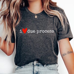 May include: Dark gray t-shirt with the text "i ❤️ due process" in white, with a red heart replacing the word "love". The shirt is a crew neck style and is made of a soft material.