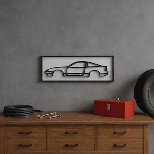 Puede incluir: Un contorno negro de coche en un marco negro cuelga de una pared gris. Una caja de herramientas roja, un neumático y herramientas están en una cómoda de madera. Una manguera negra está enrollada en la cómoda.