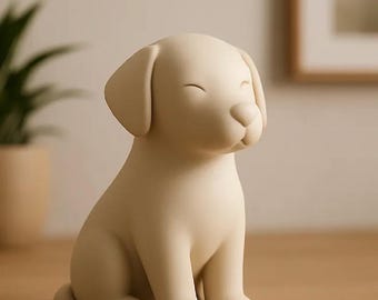 May include: A cream-colored ceramic puppy figurine in a seated position with closed eyes. The dog has floppy ears and a rounded snout. The figurine is on a wooden surface, with a blurred background including a plant and a framed picture.