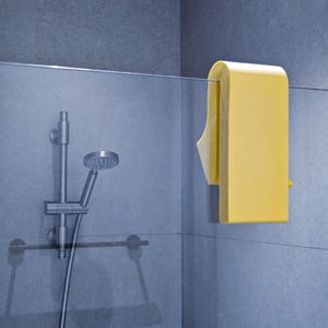 May include: A yellow shower squeegee attached to a glass shower screen. The squeegee has a rectangular shape with a curved top and a small yellow knob. A silver shower head and tap are in the background.