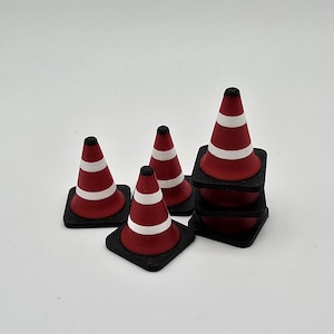 Könnte beinhalten: Eine Ansammlung von Miniatur-Leitkegeln in Rot und Weiß mit schwarzen Sockeln. Einige Kegel sind gestapelt, andere stehen einzeln. Die Kegel haben ein klassisches Design mit einem weißen Reflexband.