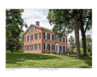 May include: A brick house with white trim and black shutters. The house has a large front porch with a red wreath on the door. The house is surrounded by green grass and trees.