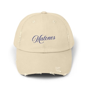 May include: A distressed, beige baseball cap with the word "Malones" embroidered in a dark blue script across the front. The cap has a curved brim and a worn, vintage look.