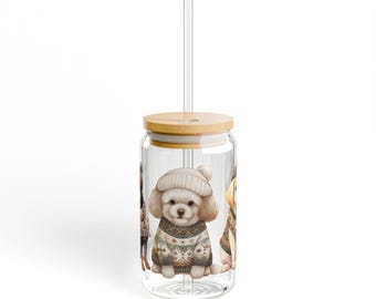 May include: A clear glass tumbler with a wooden lid and a clear straw. The tumbler features illustrations of dogs wearing sweaters and hats. The dogs are in a winter theme. The tumbler is designed for cold beverages.