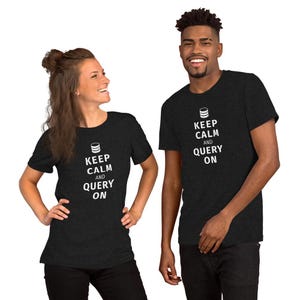 Op de afbeelding: Twee mensen dragen donkergrijze t-shirts met de tekst "KEEP CALM AND QUERY ON" in het wit. De shirts hebben ook een database-pictogram boven de tekst. Beiden lachen.