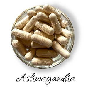 Op de afbeelding: Een glazen kom gevuld met lichtbruine capsules met het label "Ashwagandha".
