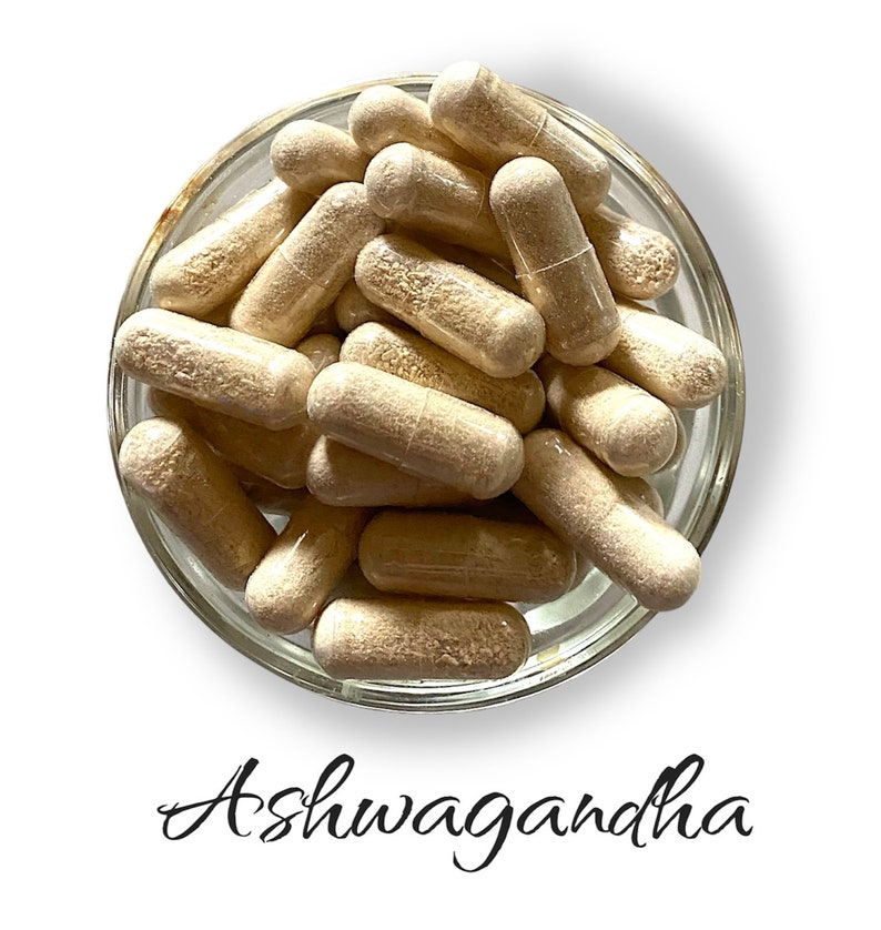 Op de afbeelding: Een glazen kom gevuld met lichtbruine capsules met het label "Ashwagandha".