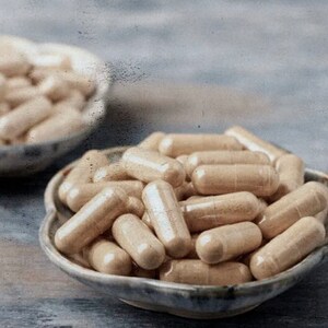 Op de afbeelding: Een close-up van twee kommen gevuld met beige capsules. De kommen zijn gemaakt van keramiek en hebben een lichtbruine glazuur. De capsules zijn in een willekeurig patroon gerangschikt.