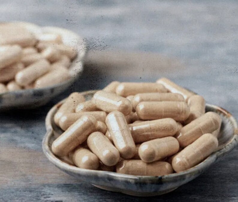 Op de afbeelding: Een close-up van twee kommen gevuld met beige capsules. De kommen zijn gemaakt van keramiek en hebben een lichtbruine glazuur. De capsules zijn in een willekeurig patroon gerangschikt.