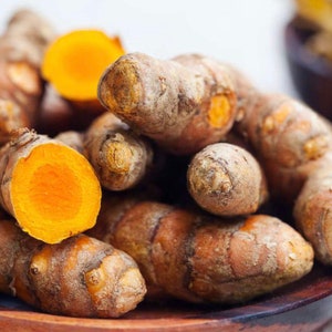 May include: A close-up of a pile of turmeric root, some of which are cut open to reveal the bright orange flesh. The turmeric is in a wooden bowl.