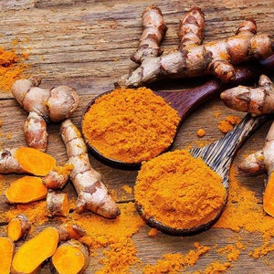 May include: Close-up of turmeric root and ground turmeric powder in wooden spoons. The turmeric root is a bright yellow color and has a rough texture. The powder is a vibrant orange color and is finely ground.