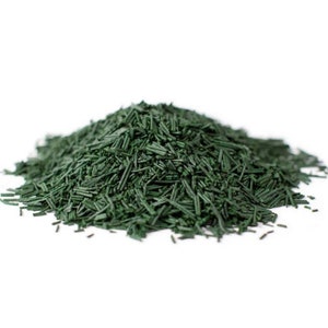 May include: A close-up of a pile of dried green spirulina powder. The powder is in the shape of small, thin strands.