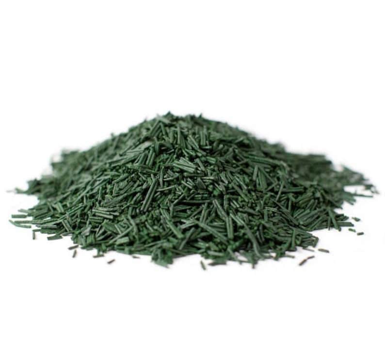 May include: A close-up of a pile of dried green spirulina powder. The powder is in the shape of small, thin strands.
