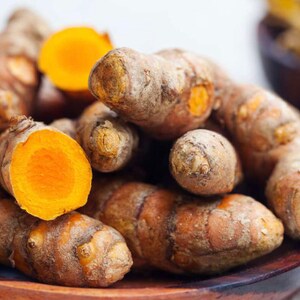 May include: A close-up of a pile of turmeric root, some of which are cut open to reveal the bright orange flesh. The turmeric is in a wooden bowl.
