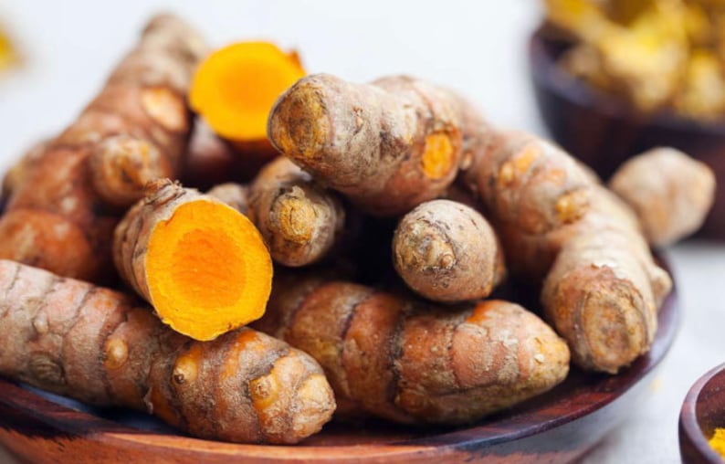 May include: A close-up of a pile of turmeric root, some of which are cut open to reveal the bright orange flesh. The turmeric is in a wooden bowl.