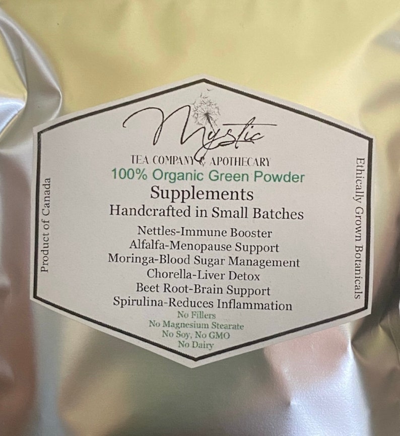 May include: A white bag with a green label that reads "Mystic Tea Company Apothecary 100% Organic Green Powder Supplements Handcrafted in Small Batches" and lists the benefits of the product, including "Nettles-Immune Booster", "Alfalfa-Menopause Support", "Moringa-Blood Sugar Management", "Chorella-Liver Detox", "Beet Root-Brain Support", and "Spirulina-Reduces Inflammation". The label also states "No Fillers", "No Magnesium Stearate", "No Soy, No GMO", and "No Dairy". The bag is labeled "Ethically Grown Botanicals" and "Product of Canada".