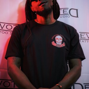 May include: A man wearing a black t-shirt with a white skull graphic and the text "Premium Quality 100% Handmade". He is wearing a black baseball cap and sunglasses.