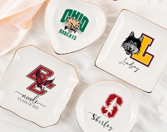 Puede incluir: Una colección de cuencos de cerámica blanca con bordes dorados. Cada cuenco presenta un logotipo y un nombre de la universidad, incluidos Ohio Bobcats, Boston College y Stanford. Los cuencos tienen varias formas, incluyendo corazón, cuadrado y redondo.