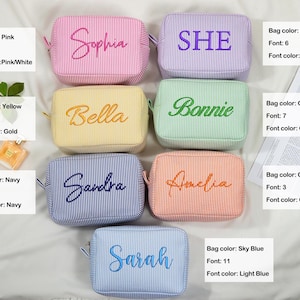 May include: A collection of personalized cosmetic bags in various colors, including pink, purple, yellow, green, orange, navy, and sky blue. Each bag features a name or word embroidered in a coordinating color, with a striped pattern.