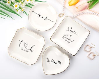 Pode incluir: Uma coleção de pratos de cerâmica brancos para anéis em várias formas: redonda, quadrada, coração e irregular. Cada prato tem uma borda dourada e escrita preta personalizada. Ideal para presentes de casamento ou aniversário.