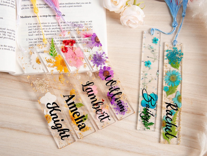 May include: Clear resin bookmarks with dried flowers and gold flakes. Each bookmark features a different name in black script: Knight, Amelia, Lambert, William, Bailey, and Rachel. Some have blue or purple tassels.