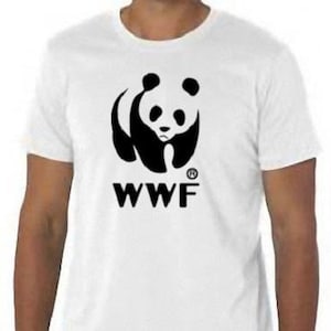 Può includere: Maglietta bianca con una grafica di un panda bianco e nero e il testo "WWF" stampato sul davanti.