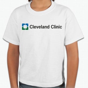以下が含まれることがあります： 白いTシャツに、青と緑のロゴが印刷されています。ロゴには「Cleveland Clinic」と書いてあります。