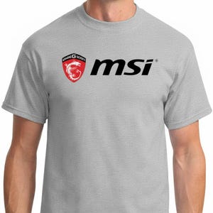 Könnte beinhalten: Hellgraues T-Shirt mit dem schwarzen MSI-Logo und einem rot-weißen Drachenemblem. Das T-Shirt hat einen Rundhalsausschnitt und kurze Ärmel. Der Text "GAMING G SERIES" befindet sich über dem Drachenemblem.