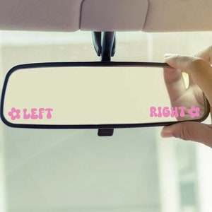 May include: A black rearview mirror with pink flower stickers that say "LEFT" and "RIGHT" on either side of the mirror.