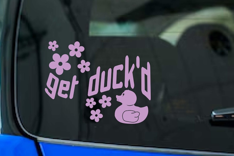 May include: A light purple vinyl decal with the phrase "get duck'd" and a cartoon duck illustration. The decal also features several small flower graphics. The decal is designed to be applied to a car window.