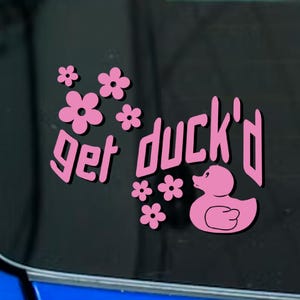 May include: Pink sticker with the phrase "get duck'd" in a stylized font, accompanied by pink flowers and a duck illustration. The sticker is designed to be applied to a car window or similar surface.