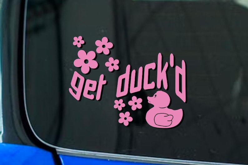 May include: Pink sticker with the phrase "get duck'd" in a stylized font, accompanied by pink flowers and a duck illustration. The sticker is designed to be applied to a car window or similar surface.