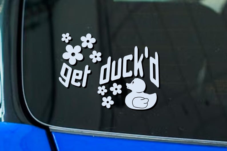 May include: White sticker with the phrase "get duck'd" in a stylized font, accompanied by a cartoon duck and several white flower graphics. The sticker is designed to be applied to a car window or similar surface.