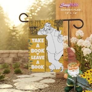 Puede incluir: Una bandera de jardín amarilla con una ilustración en blanco y negro de una persona sosteniendo un libro. El texto en la bandera dice "Take a Book Leave a Book".