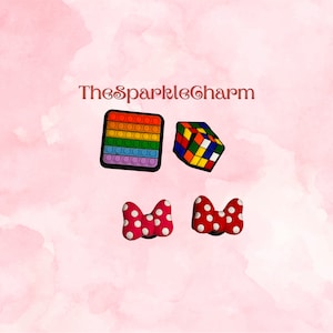 May include: Four colorful shoe charms: a rainbow pop-it, a Rubik's cube, and two red bows with white polka dots.