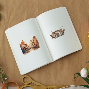 Pode incluir: Um caderno aberto com duas ilustra&ccedil;&otilde;es de aquarela. A p&aacute;gina da esquerda apresenta uma cena de rua com edif&iacute;cios e pessoas. A p&aacute;gina da direita mostra um edif&iacute;cio com um telhado pontudo e janelas arqueadas.