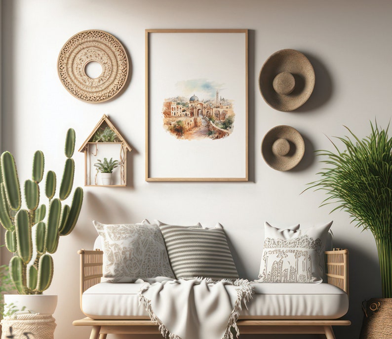Op de afbeelding: Een witte bank met een wit dekentje en drie kussens. De kussens zijn versierd met een bloemenpatroon, strepen en een geometrisch patroon. De bank staat voor een witte muur met een ingelijst aquarel schilderij van een stadssc&egrave;ne, een ronde geweven wanddecoratie en twee geweven hoeden.