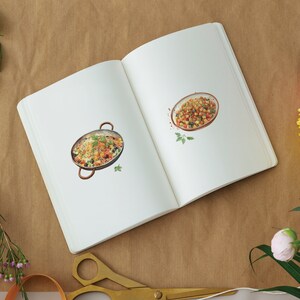 May include: An open notebook with two watercolor illustrations of bowls of food. The first bowl contains a yellow rice dish with vegetables. The second bowl contains a colorful salad with red, yellow, and green ingredients.