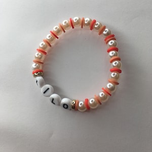 May include: A white pearl bracelet with orange and red beads spelling out the word "I LOVE" in white letters.