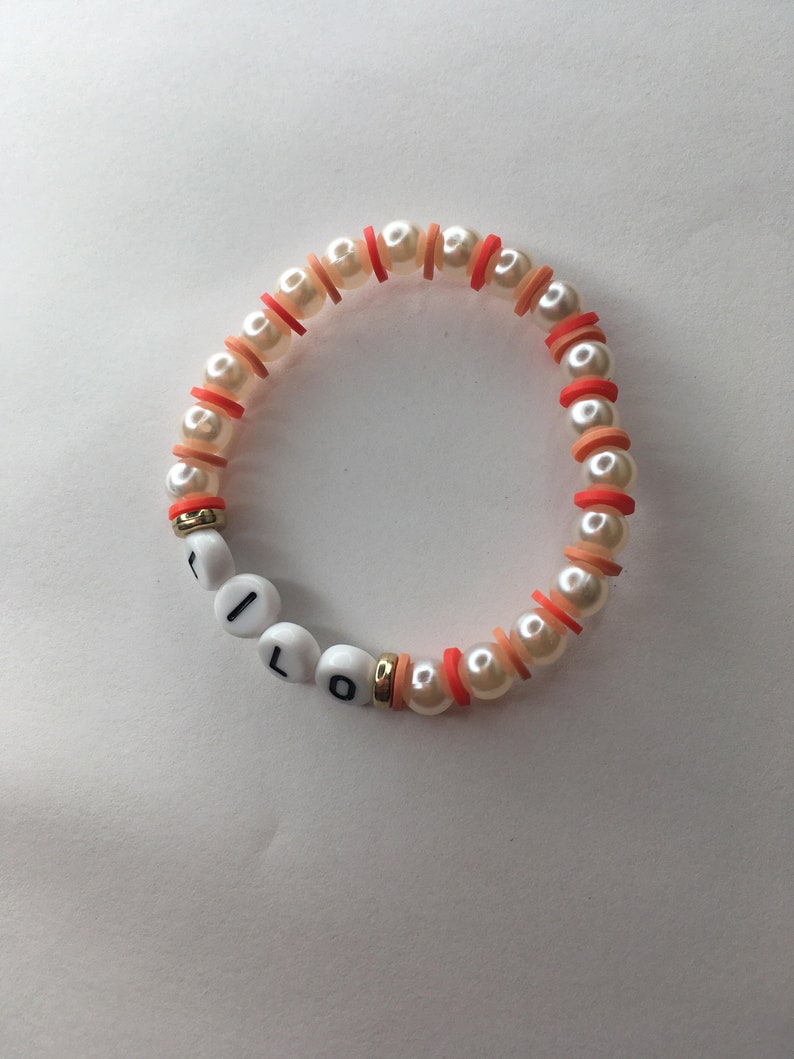 May include: A white pearl bracelet with orange and red beads spelling out the word "I LOVE" in white letters.