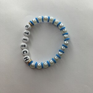 May include: White pearl bracelet with blue accents and the word "STITCH" spelled out in black letters.