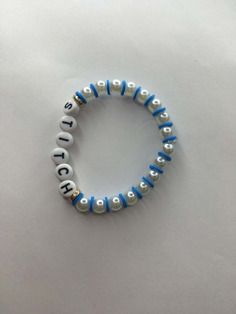 May include: White pearl bracelet with blue accents and the word "STITCH" spelled out in black letters.