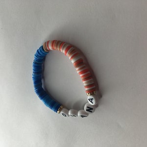 May include: A colorful bracelet made of blue, white, and orange beads with the word "ANA" spelled out in white letters on the bracelet.
