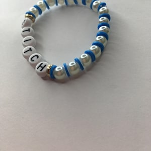 May include: White beaded bracelet with blue accents and the word "Stitch" spelled out in white beads.