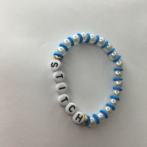 May include: White beaded bracelet with blue accents and the word "STITCH" spelled out in black letters on white beads.