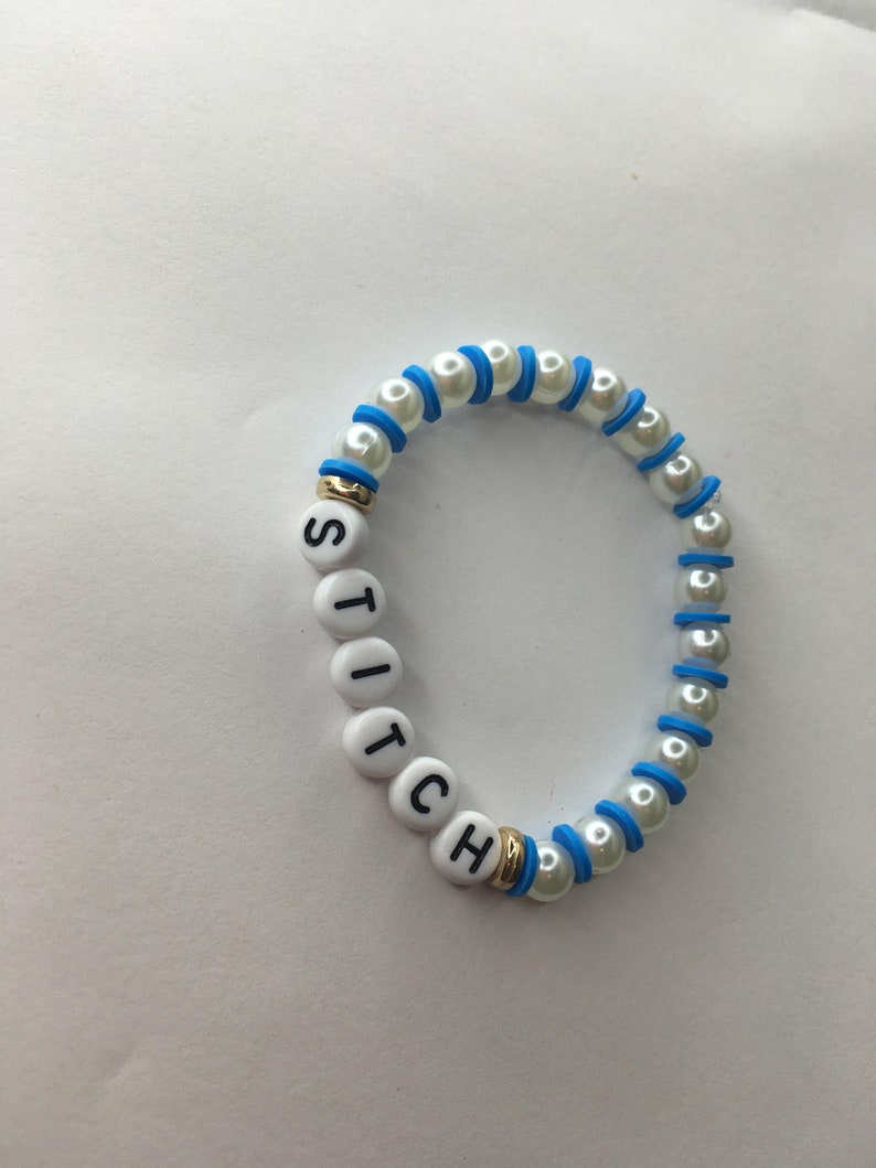 May include: White beaded bracelet with blue accents and the word "STITCH" spelled out in black letters on white beads.