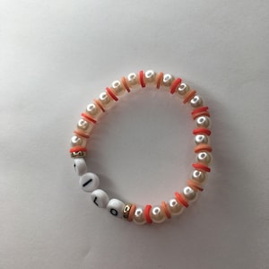May include: A white pearl bracelet with red and orange beads spelling out the word "LOL".