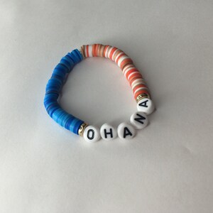 May include: A blue, white, and orange beaded bracelet with the word "OHANA" spelled out in white beads with black lettering.