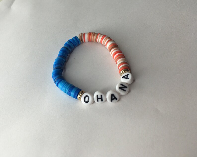 May include: A blue, white, and orange beaded bracelet with the word "OHANA" spelled out in white beads with black lettering.